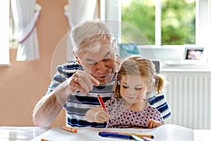 Cute little baby toddler girl and handsome senior grandfather painting with colorful pencils at home. Grandchild and man