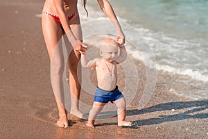 Cute little baby walking along the seaside with his sister