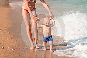 Cute little baby walking along the seaside with his sister