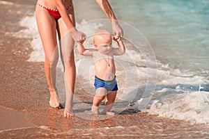 Cute little baby walking along the seaside with his sister