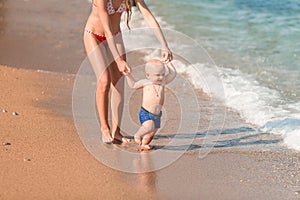 Cute little baby walking along the seaside with his sister