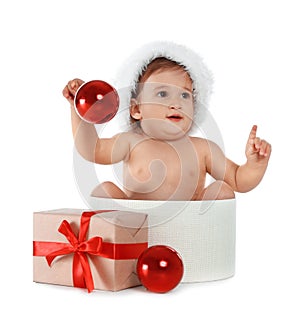 Cute little baby wearing Santa hat sitting in box with Christmas gift on background