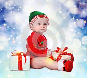 Cute little baby wearing Santa`s elf clothes with Christmas gifts on color background