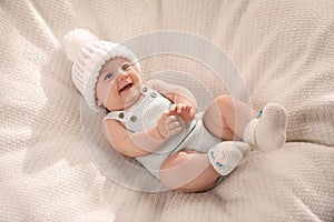 Cute little baby wearing white warm hat on knitted blanket