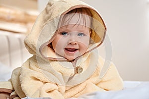 Cute little baby in yellow hooded towel on bed after bath