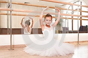 Cute little ballerina standing with her hands up in a performance dress. She is dreaming to become a professional ballet dancer.