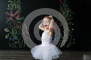 Cute little ballerina in white ballet costume is dancing in the room. Kid in dance class.