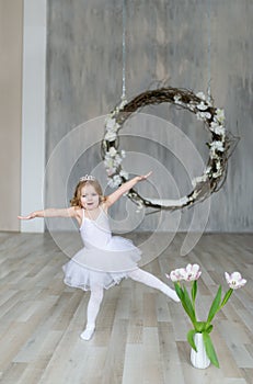 Cute little ballerina in white ballet costume is dancing in the room. Kid in dance class.