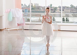 Cute little ballerina in white ballet costume and pointe shoes with is dancing in the room