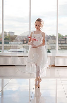 Cute little ballerina in white ballet costume and pointe shoes with is dancing in the room