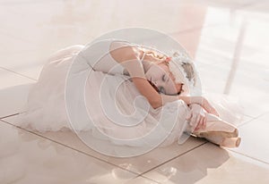 Cute little ballerina in white ballet costume and pointe shoes is posing on floor