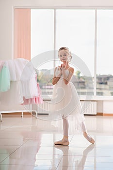 Cute little ballerina in white dress and pointe shoes dreams about ballet dances