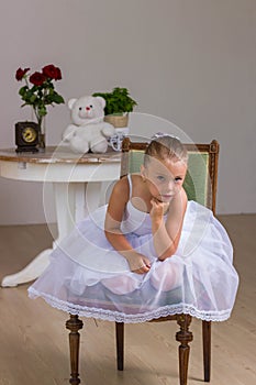 Cute little ballerina in a white dress sitting