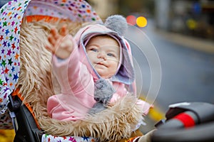 Cute little beautiful baby girl sitting in the pram or stroller on autumn day. Happy smiling child in warm clothes
