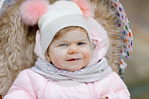 Cute little beautiful baby girl sitting in the pram or stroller on cold autumn, winter or spring day. Happy smiling