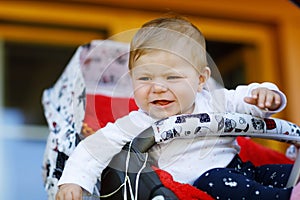 Cute little beautiful baby girl sitting in the pram or stroller and waiting for mom. Crying sad child with blue eyes.