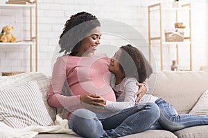 Cute little black girl and her pregnant mom embracing at home