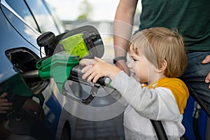 Cute little blond boy holding pump nozzle. Small funny kid helping father to fuel the car at a gas station