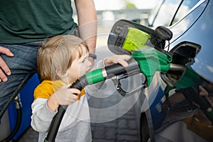 Cute little blond boy holding pump nozzle. Small funny kid helping father to fuel the car at a gas station