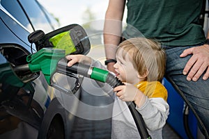 Cute little blond boy holding pump nozzle. Small funny kid helping father to fuel the car at a gas station