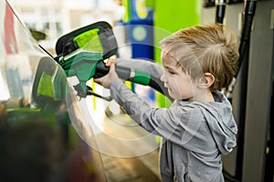 Cute little blond boy holding pump nozzle. Small kid helping father to fuel the car at a gas station. Daddy\'s little helper