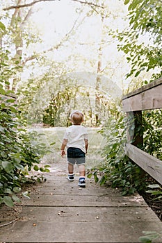 Cute Little Blond Boy Kid Walking on Tiny Wooden Bridge Outside at the Park while Exploring on an Adventure in New York Summer