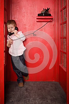 Cute little blond boy in a pink shirt and jeans call on the retro telephone in a British telephone box. old telephone
