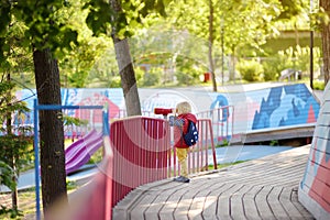 Cute little blond caucasian boy, kid or child looking through binoculars on playground outdoors