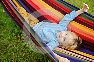 Cute little blond caucasian boy relaxing and having fun in multicolored hammock in backyard or outdoor playground. Summer active