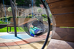 Cute little blond caucasian boy relaxing and having fun in multicolored hammock in backyard or outdoor playground. Summer active