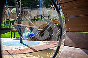 Cute little blond caucasian boy relaxing and having fun in multicolored hammock in backyard or outdoor playground. Summer active