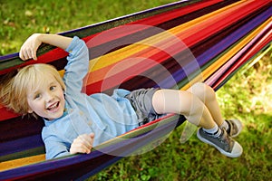 Cute little blond caucasian boy relaxing and having fun in multicolored hammock in backyard or outdoor playground. Summer active