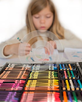 Cute little blond girl is drawing by colorful pencils , box of pencils on the foreground