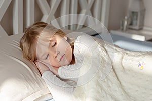 Cute little blond toddler girl sleeping in bed.Sweet baby lying with closed eyes under rays of sun at sunrise in early