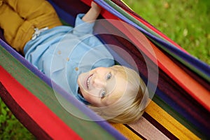 Cute little blond white boy enjoy and having fun with multicolored hammock in backyard or outdoor playground. Summer outdoors