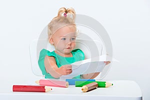 Cute little blonde baby girl 1 year old is drawing with big colored pencils isolated on white background. Early development from