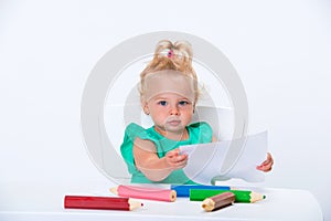 Cute little blonde baby girl 1 year old is drawing with big colored pencils isolated on white background. Early development from