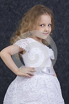 Cute little blonde girl in a beautiful white dress on a dark background