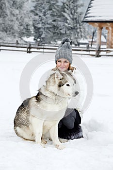 Cute little blonde girl playing in the snow with a dog Husky