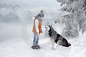 Cute little blonde girl playing in the snow with a dog Husky