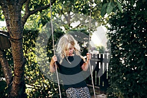 Cute little blonde girl playing on a tree swing outside