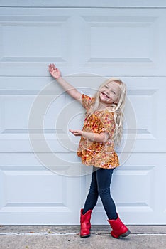 Cute little blonde girl standing in the driveway in red cowboy boots