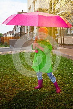 Cute little blonde girl with umbrella under rain drops on lawn in a sunny summer day