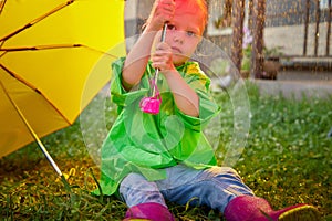 Cute little blonde girl with umbrella under rain drops on lawn in a sunny summer day