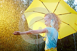 Cute little blonde girl with umbrella under rain drops on lawn in a sunny summer day