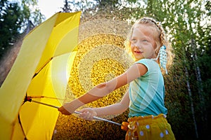 Cute little blonde girl with umbrella under rain drops on lawn in a sunny summer day