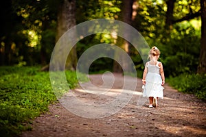 Cute little blonde girl in a white dress walking down the path i