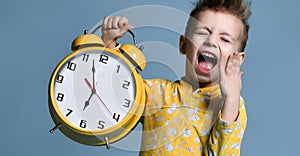 Cute little boy with alarm clock,isolated on blue. Funny kid pointing at alarm clock at 7 o`clock at morning.