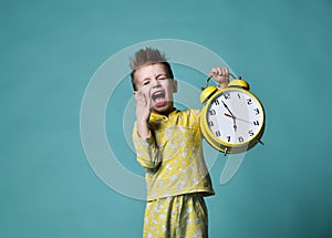 Cute little boy with alarm clock,isolated on blue. Funny kid pointing at alarm clock at 7 o`clock at morning.