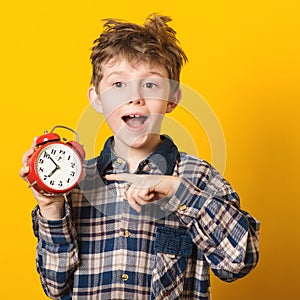 Cute little boy with alarm clock,isolated on yellow. Funny kid pointing at alarm clock at 7 o `clock at morning. Excited boy overs